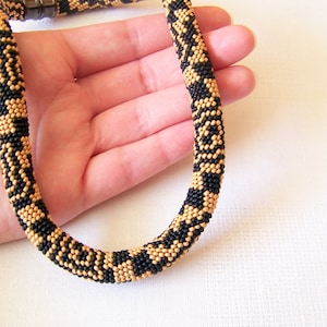 May include: A black and gold beaded necklace with a geometric pattern. The necklace is made of small beads and is about 18 inches long.