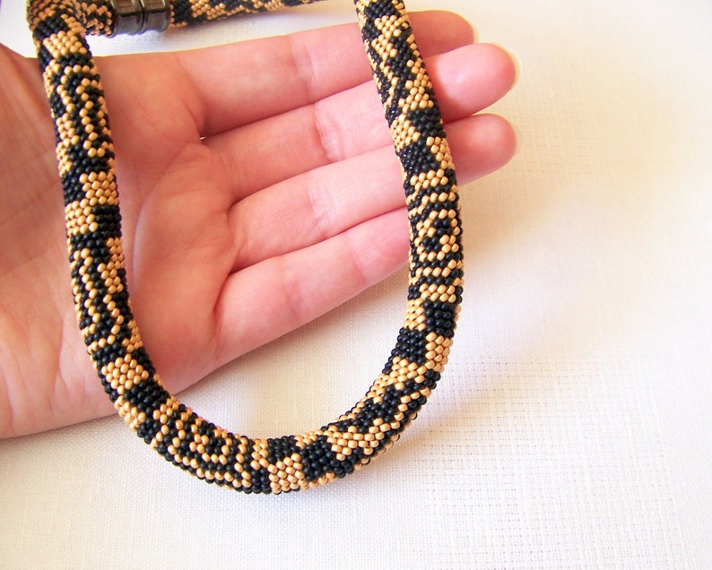 May include: A black and gold beaded necklace with a geometric pattern. The necklace is made of small beads and is about 18 inches long.