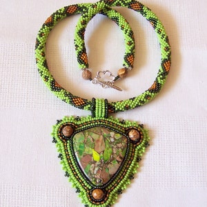 May include: A green and brown beaded necklace with a triangular pendant featuring a green and brown stone.