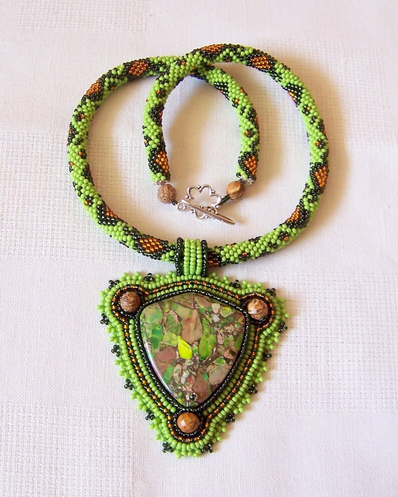 May include: A green and brown beaded necklace with a triangular pendant featuring a green and brown stone.