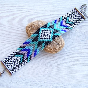 Puede incluir: Un brazalete de cuentas con un patr&oacute;n geom&eacute;trico en negro, blanco, azul, turquesa y rosa. El brazalete tiene un cierre plateado.