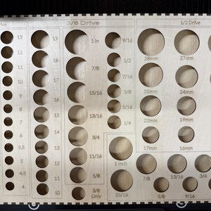 May include: A light-colored wooden socket organizer tray featuring laser-cut circular holes for various tool sizes. The board is divided into sections labeled 1/4 Drive, 3/8 Drive, and 1/2 Drive, with corresponding imperial and metric size markings printed next to each hole.
