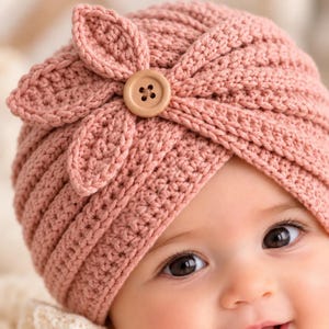 May include: A dusty rose crochet hat featuring a textured ribbed pattern and a decorative flower accent on the side. The center of the flower is adorned with a round, light brown wooden button with four small holes in the middle.