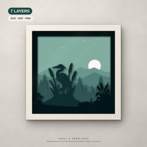 Puede incluir: Una pieza de arte en papel recortado de 7 capas en un marco cuadrado que muestra la silueta de una garza entre espada&ntilde;as, monta&ntilde;as y una luna llena en tonos verde azulado y verde. El texto 7 LAYERS SVG DXF PNG y FJELL & FERN CUTS.