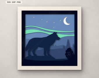 May include: A seven-layer paper cut art piece in a square frame featuring a dark blue wolf silhouette standing before a landscape with light green aurora borealis, a white crescent moon, and stars against a blue sky. Text reads 7 LAYERS.