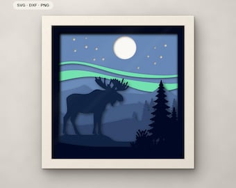 May include: A square framed 7-layer paper art piece featuring a dark blue moose silhouette standing in a forest landscape under a light blue sky with a white moon, stars, and green aurora borealis. Text includes 7 LAYERS, SVG, DXF, PNG, and FJELL & FERN CUTS.