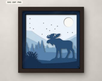 May include: A square framed multi-layered paper art piece featuring a dark blue moose silhouette in a forest landscape with mountains, a moon, and stars. The text 7 LAYERS, SVG, DXF, PNG, and FJELL & FERN CUTS is visible.