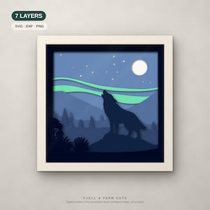 Op de afbeelding: Een zevenlaags papierkunstwerk in een vierkante lijst met een donkerblauw silhouet van een huilende wolf op een rots. De sc&egrave;ne bevat een lichtblauwe lucht met een witte maan, kleine ronde sterren en groene noorderlichtgolven.