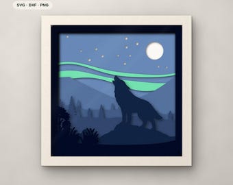 May include: A seven-layer paper cut art piece in a square frame featuring a dark blue silhouette of a wolf howling on a rock. The scene includes a light blue sky with a white moon, small circular stars, and green aurora borealis waves.