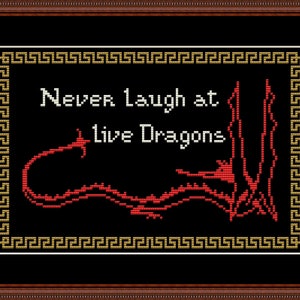May include: Cross-stitch art framed in a brown wooden frame. The black background features the text "Never Laugh at live Dragons" in white, with a red dragon design. The frame has a gold Greek key border.