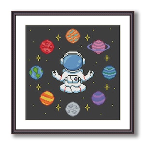 Puede incluir: Un patrón de punto de cruz que presenta un astronauta meditando en el espacio rodeado de planetas. El astronauta lleva un traje espacial blanco con un casco azul. Los planetas son de varios colores, incluyendo rojo, naranja, amarillo, verde, azul y morado.