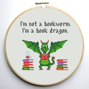 May include: Cross stitch pattern featuring a green dragon holding a red book, with the text "I'm not a bookworm. I'm a book dragon."
