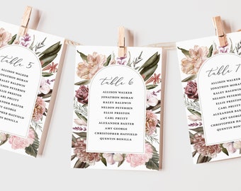 May include: Three floral wedding table cards with guest names and table numbers 5, 6, and 7. The cards feature a watercolor floral design in shades of pink, burgundy, and green, with an arched frame around the table number.