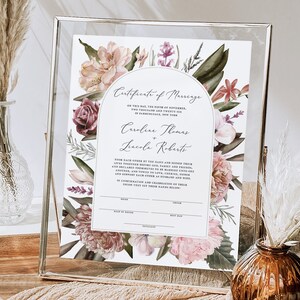 May include: A printable wedding certificate with a floral border. The certificate is white with black text and the names "Caroline Thomas" and "Lincoln Roberts" are printed in cursive. The floral border features pink, purple, and green flowers.