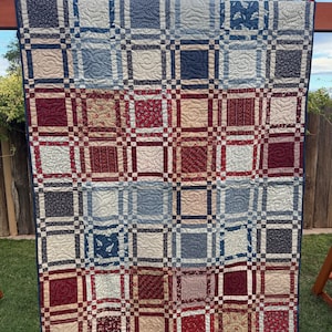 May include: A patchwork quilt featuring a grid of square fabric blocks in shades of navy blue, cream, and deep red. The quilt displays various floral and geometric patterns with intricate swirling machine-stitched quilting throughout the surface.