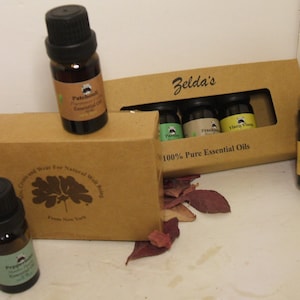 May include: A set of six small brown glass bottles with black caps containing essential oils. The bottles are arranged in a brown cardboard box with the text "Zelda's 100% Pure Essential Oils".