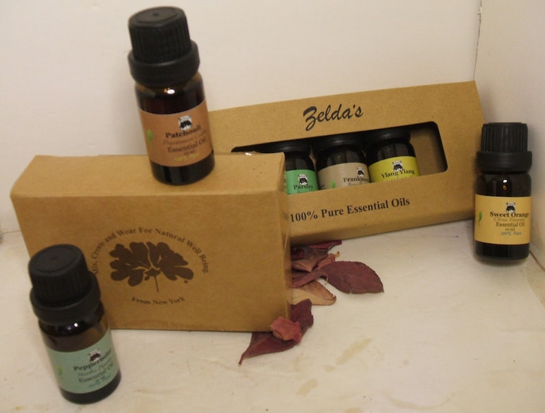 May include: A set of six small brown glass bottles with black caps containing essential oils. The bottles are arranged in a brown cardboard box with the text "Zelda's 100% Pure Essential Oils".