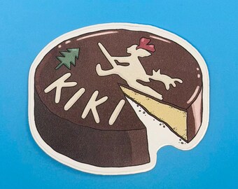 May include: A die-cut sticker shaped like a round chocolate cake with a slice removed. The top features the text KIKI in white, a small green pine tree, and a white silhouette of a figure on a broomstick with a red bow.