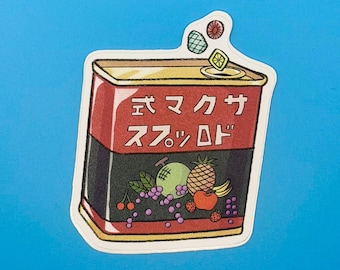 May include: A rectangular sticker of a red and black tin can featuring Japanese text, with illustrations of various fruits including grapes, a melon, a pineapple, and cherries, and small fruit-shaped candies floating above the open top.
