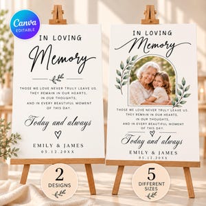 May include: Two white memorial signs on wooden easels featuring black text that reads In Loving Memory, Today and always, and the names Emily & James with a date. One sign includes a photo of an older person and a child framed by green leaves.