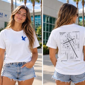 May include: A white short-sleeve t-shirt featuring a small blue eagle graphic on the front left chest and a large black and white airport diagram print on the back, including the text "AIRPORT DIAGRAM" and "DAYTONA BEACH INTL".