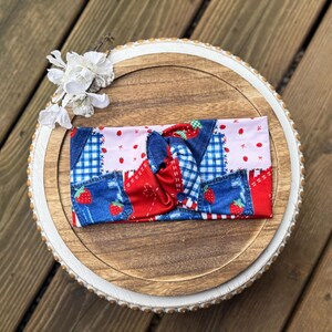 Puede incluir: Una colorida diadema con un diseño de patchwork. La diadema presenta telas vaqueras, rojas y rosas, con estampados de fresas y cuadros vichy. El diseño anudado añade un toque elegante a este accesorio.