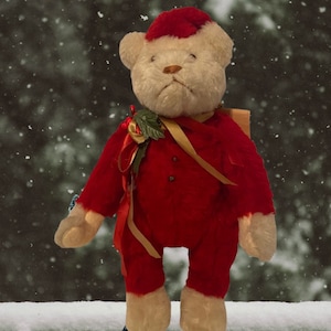 Op de afbeelding: Een vintage teddybeer met een rood kerstmanpak en -muts, met hulst en gouden lint. De beer heeft een crèmekleurig gezicht, poten en voeten. De achtergrond is een besneeuwde bosscène.