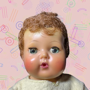 May include: A vintage baby doll with light brown hair and blue-green eyes. The doll has rosy cheeks and a slightly open mouth. It is wearing a light yellow outfit. The background is a pink color with colorful geometric shapes.