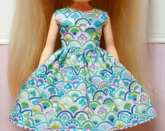May include: A white dress with a green, blue, and purple geometric pattern. The dress has a full skirt and sleeveless bodice.