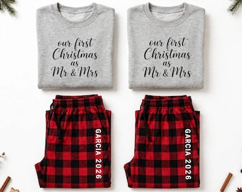 May include: Two sets of matching pajamas featuring grey crewneck sweatshirts with the black text 'our first Christmas as Mr & Mrs' and red and black buffalo plaid pajama pants with the white text 'GARCIA 2026' printed vertically on the leg.