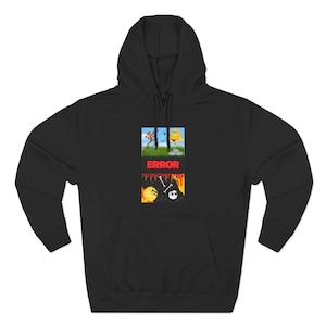 May include: A black hooded sweatshirt featuring a central graphic design. The design shows a split scene with a sunny grassy landscape above and a dark fiery scene with bones and a skull below, separated by the red text ERROR.