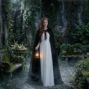 May include: A floor-length white dress paired with a long black hooded cloak featuring a black ribbon tie at the neck. The cloak is worn over the dress, which has a fitted bodice and a flowing skirt. A lit lantern is held in one hand.