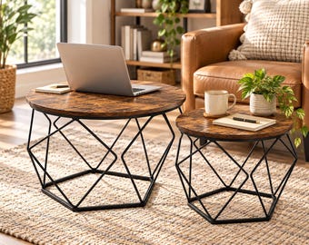 May include: A set of two round nesting coffee tables featuring dark brown wood-grain tops and black geometric metal wire bases. The larger table holds a silver laptop and a notebook, while the smaller table holds a white mug and a notebook.