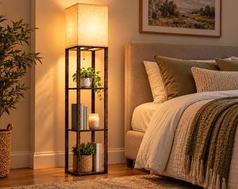 May include: A tall, rectangular floor lamp with a dark brown, wood-grain finish frame and three open storage shelves. The lamp features a square, off-white fabric shade at the top, emitting a warm, soft glow, with a pull-chain switch.
