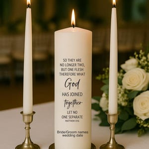 May include: A unity candle set with a central pillar candle and two taper candles. The pillar candle has the text "So they are no longer two, but one flesh therefore what God has joined together, let no one separate." The candles are ivory and gold.