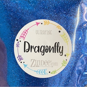 May include: A close-up of a blue glitter with a white circle label that says "Ultrafine Dragonfly. Zindee.com" with colorful arrows around the edge.
