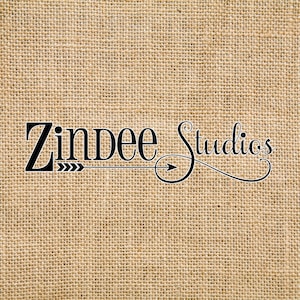May include: The words "Zindee Studios" are displayed in black script on a burlap background. The word "Zindee" has an arrow design pointing to the right, and the word "Studios" has a decorative flourish.