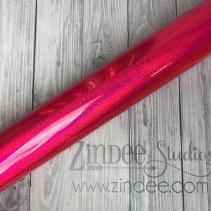 Puede incluir: Un rollo de vinilo rosa iridiscente con un acabado brillante. El vinilo est&aacute; enrollado y tiene una ligera curva. El vinilo est&aacute; sobre una superficie de madera.