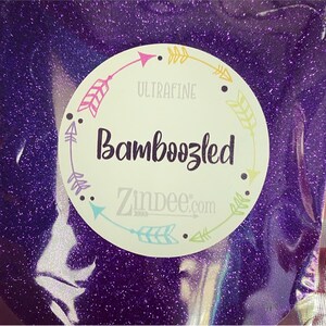 May include: A close-up of a purple glitter with a white circle label that says "Ultrafine Bambozzled Zindee.com" with a border of colorful arrows.