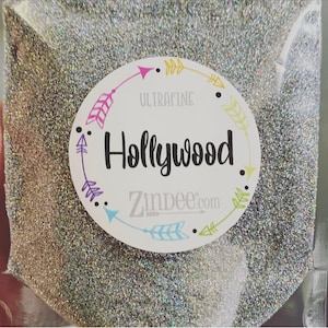 May include: A close-up of a silver glitter with a white label that says "Ultrafine Hollywood Zindee.com" with colorful arrows around the text.