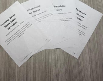 May include: Four white printed paper guides for seniors, including a Samsung Galaxy Phone Guide, an iPhone Guide, a Safety Guide, and a Facebook & Instagram Guide. Each document features black text with titles and instructional content for mobile devices.