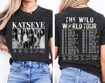 May include: A charcoal gray t-shirt featuring a front graphic of the group KATSEYE with six individual portraits and signatures. The back displays The Wild World Tour text, a list of tour dates and cities, and the members' signatures.