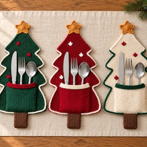 May include: Three knitted Christmas tree-shaped cutlery holders in dark green, deep red, and cream. Each features a brown trunk, a yellow star topper, and a front pocket containing a silver knife, fork, and spoon set.