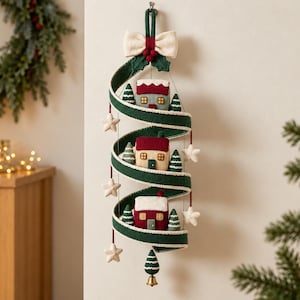May include: A vertical hanging decoration featuring a spiraling dark green felt ribbon adorned with three small fabric houses, miniature green felt pine trees, and cream-colored felt stars. A cream bow and red berries top the structure.