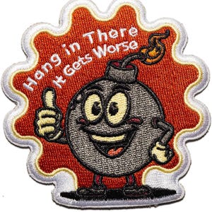May include: An embroidered patch featuring a cartoon bomb character with a smiling face and a thumbs-up gesture. The bomb is set against a red, cloud-shaped background with white borders. The text reads, "Hang in There It Gets Worse."
