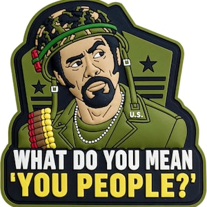 May include: A rubber morale patch featuring a cartoon soldier with a beard, wearing a camouflage helmet and a green uniform with a bullet belt. The text reads WHAT DO YOU MEAN 'YOU PEOPLE?' in white and yellow against a dark green background.