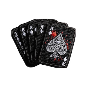 May include: A set of five black embroidered patches shaped like playing cards. The cards feature white text and symbols, including a Joker, an eight of clubs, an eight of spades, an ace of clubs, and an ace of spades with a skull and red splatter.