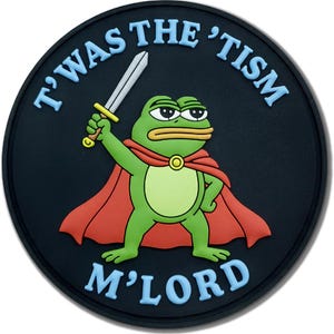 May include: A circular black patch featuring a green frog character wearing a red cape and holding a silver sword. The text T'WAS THE 'TISM M'LORD is printed in light blue letters around the top and bottom edges of the circular design.