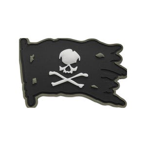 May include: A rectangular morale patch shaped like a tattered flag in matte black with a dark olive green border. The center features a white skull and crossbones emblem. The surface has a textured finish with small, irregular cutouts.