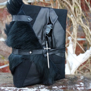 May include: A black leather journal with a fur trim and a silver dagger attached to the front.